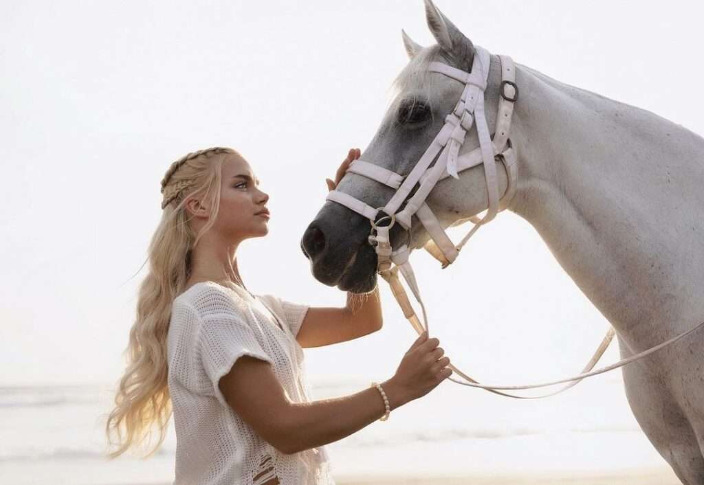 Alice Swifty is wearing white t shirt and holding the bridle of horse and posing while taking the picture
