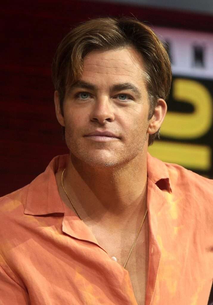 Chris Pine in the orange dress shirt pair with chain necklace while looking towards camera
