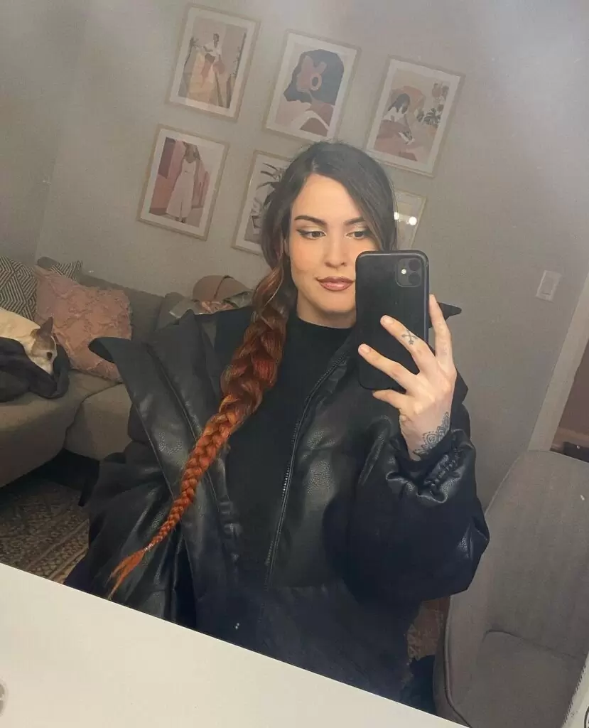 Steph Oshiri is wearing black shirt over jacket and taking selfie while standing in front of mirror