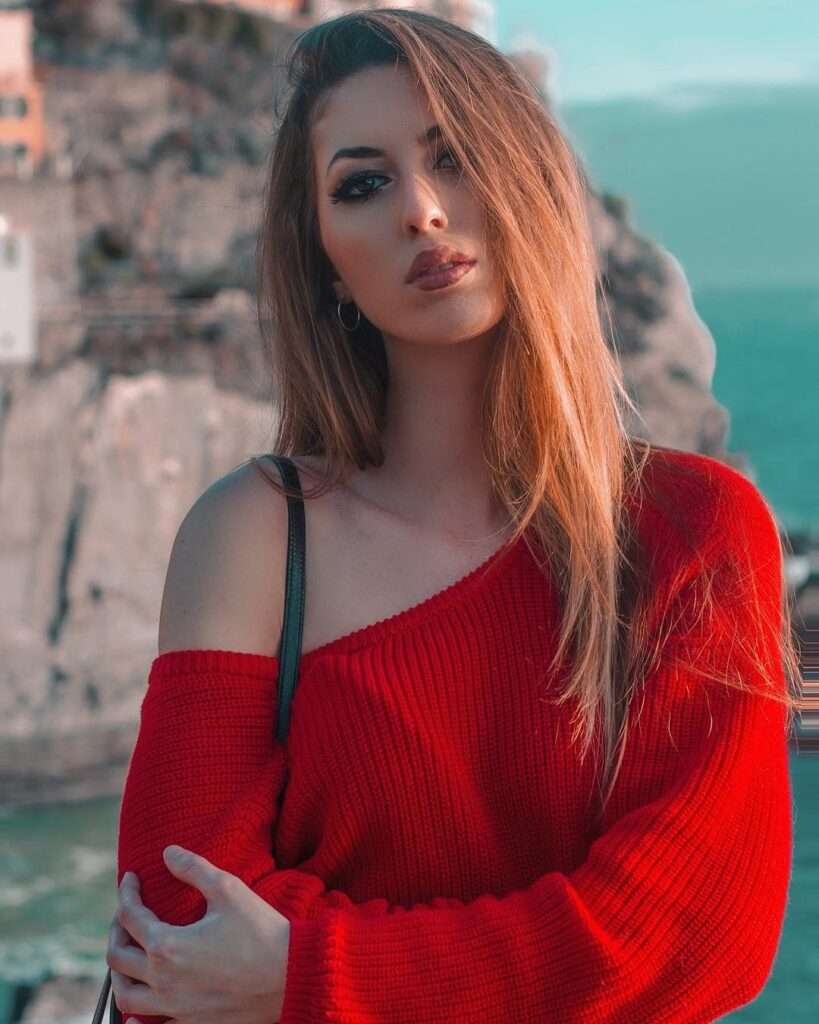 Eva Menta in the red wool top with wide neckline while smiling towards camera