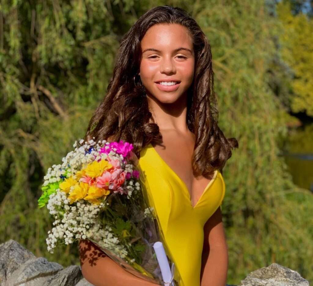 Jades Hannah in the captivating yellow outfit while holding a bouquet in her hands while smiling towards camera