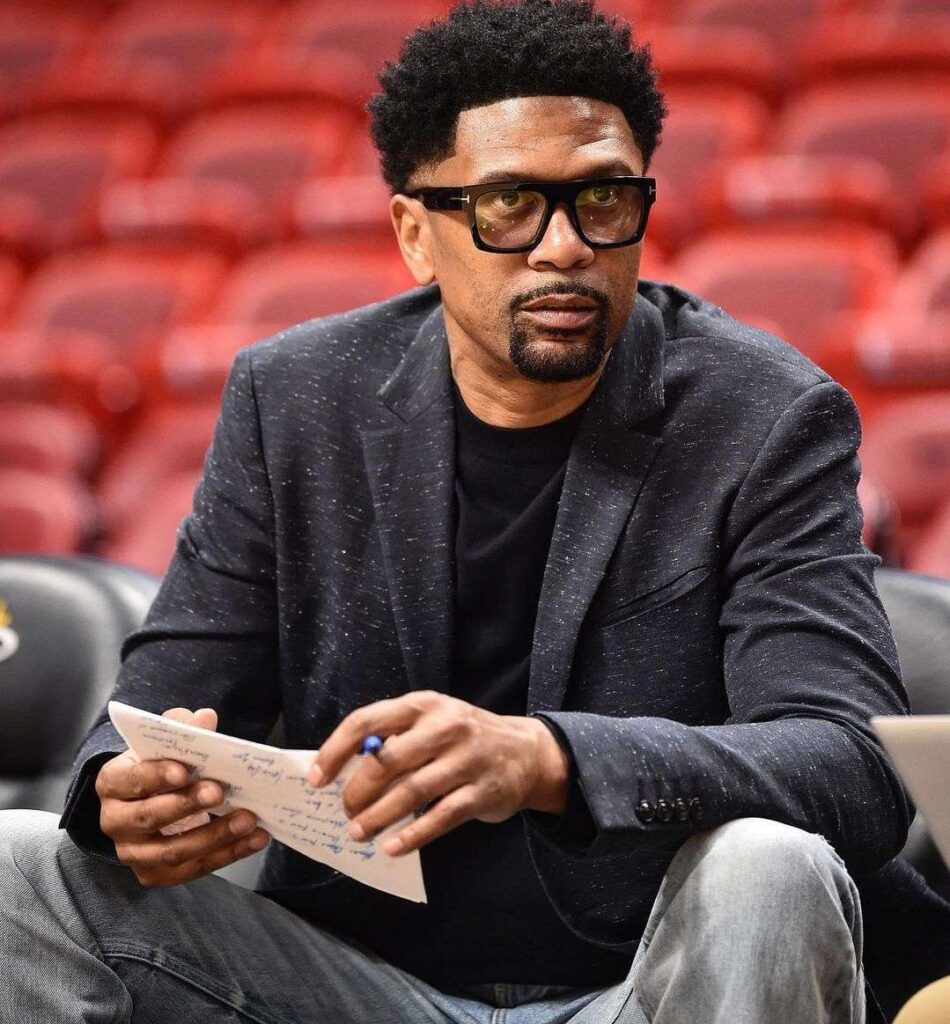 Jalen Rose in the grey 3-piece suit pair with glasses while looking towards camera and poses for a photo