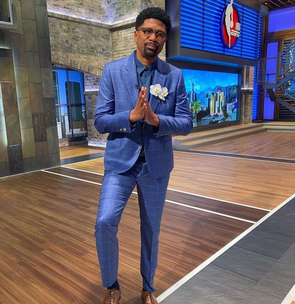Jalen Rose in the blue 3-piece suit pair with brown shoes while putting his right foot on the football