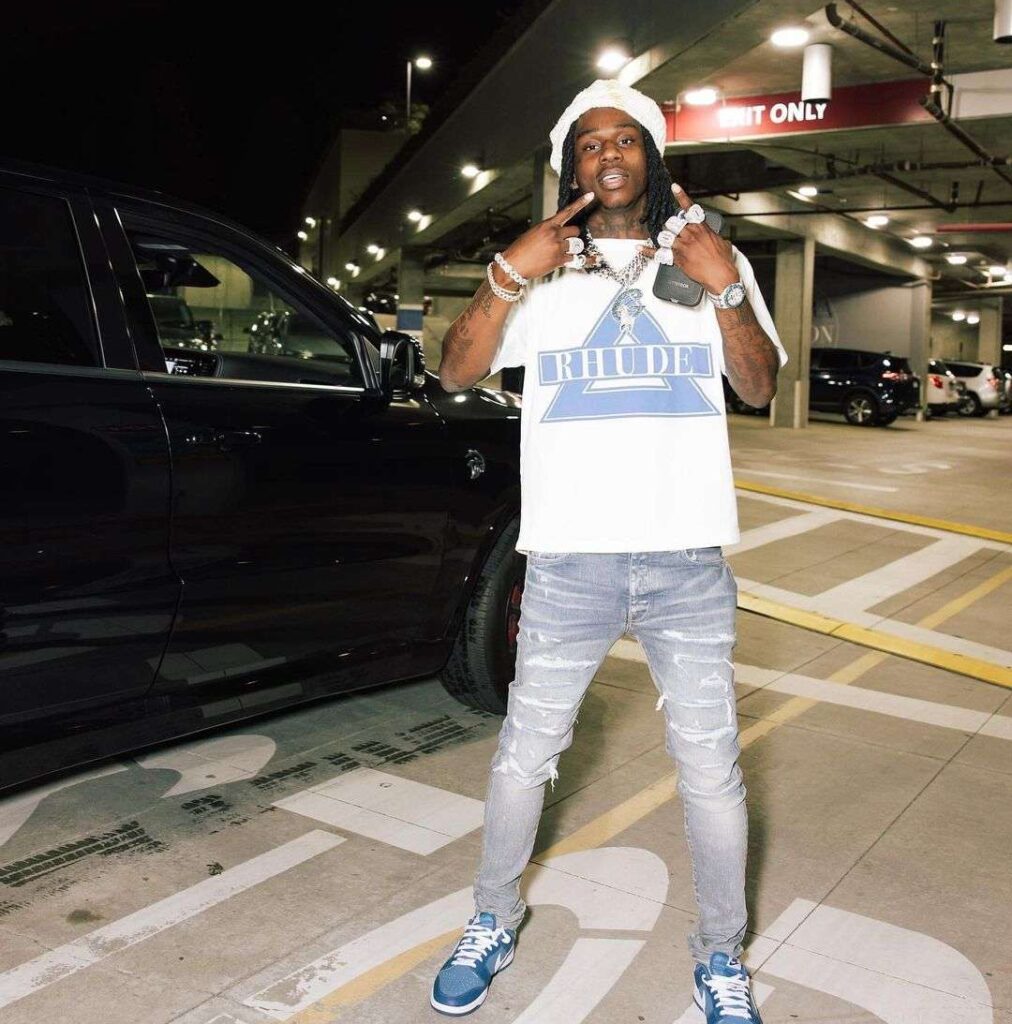 Polo G in the white t-shirt pair with blue jeans and blue sneakers while poses for a photograph