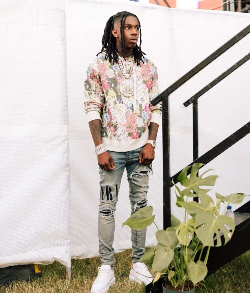 Polo G in the printed sweat shirt pair with blue jeans, white jogger, and white sneakers while poses for a photo