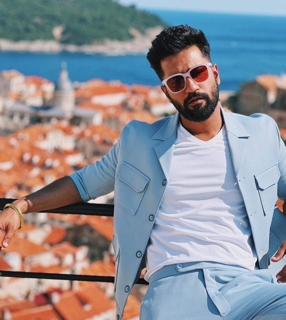 Vicky Kaushal in the white v-shaped shirt pair with sky blue coat and dress shirt while taking picture in the outdoors