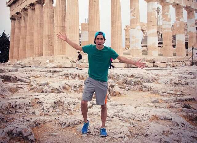 Zach king in the green t-shirt pair with grey shorts, green cap, and blue joggers while poses for a picture