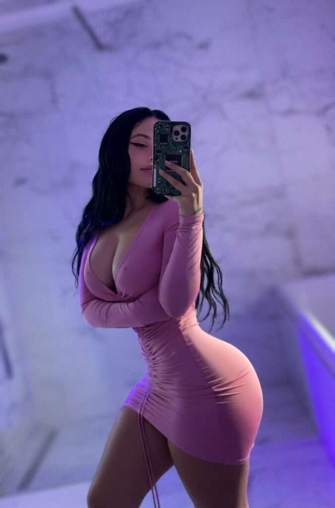 Gina Savage is wearing pink dress and standing in front of mirror while taking the picture