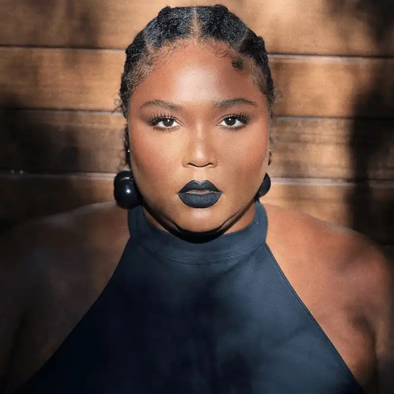 Lizzo is wearing black dress and earrings or posing while taking sun kissed for the picture