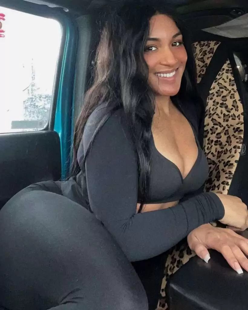 Lady Tarzán viste un traje negro, está sentada en el auto y sonríe mientras posa para la foto.