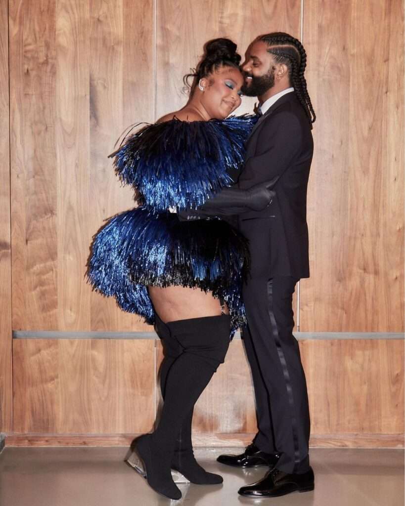 Lizzo is wearing blue shinny dress or standing with his boyfriend while posing for the picture