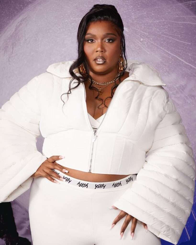 Lizzo is wearing white shirt over pant and chain or posing while taking the picture