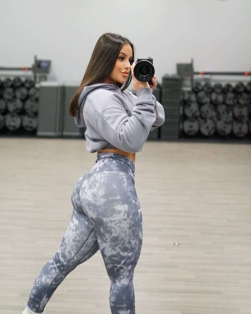Amber Loft is taking her picture while wearing a hoodie with leggings.