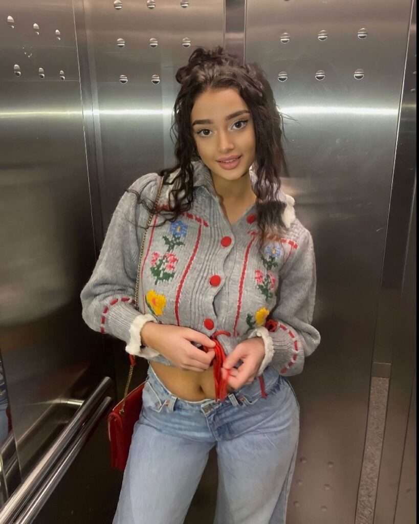 Matiana Ejupi in the grey front button top pair with blue jeans while taking photo in the lift