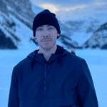Bryce Chudak in the black waterproof hoodie pair with matching cap while smiling toward camera