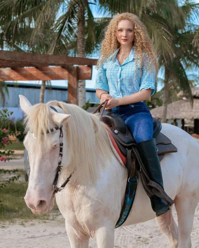 Nivea Cavalcante is sitting on a horse and is posing for a picture while wearing pant-shirt.