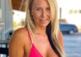 Ainslee Divine is wearing pink dress and smiling while posing for taking the picture