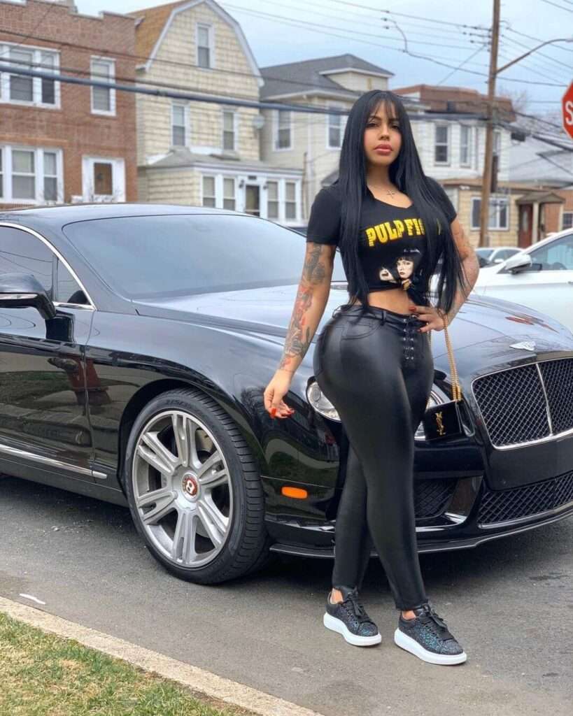 Ink Doll is wearing black t shirt and pant or standing in front of car while posing for the picture