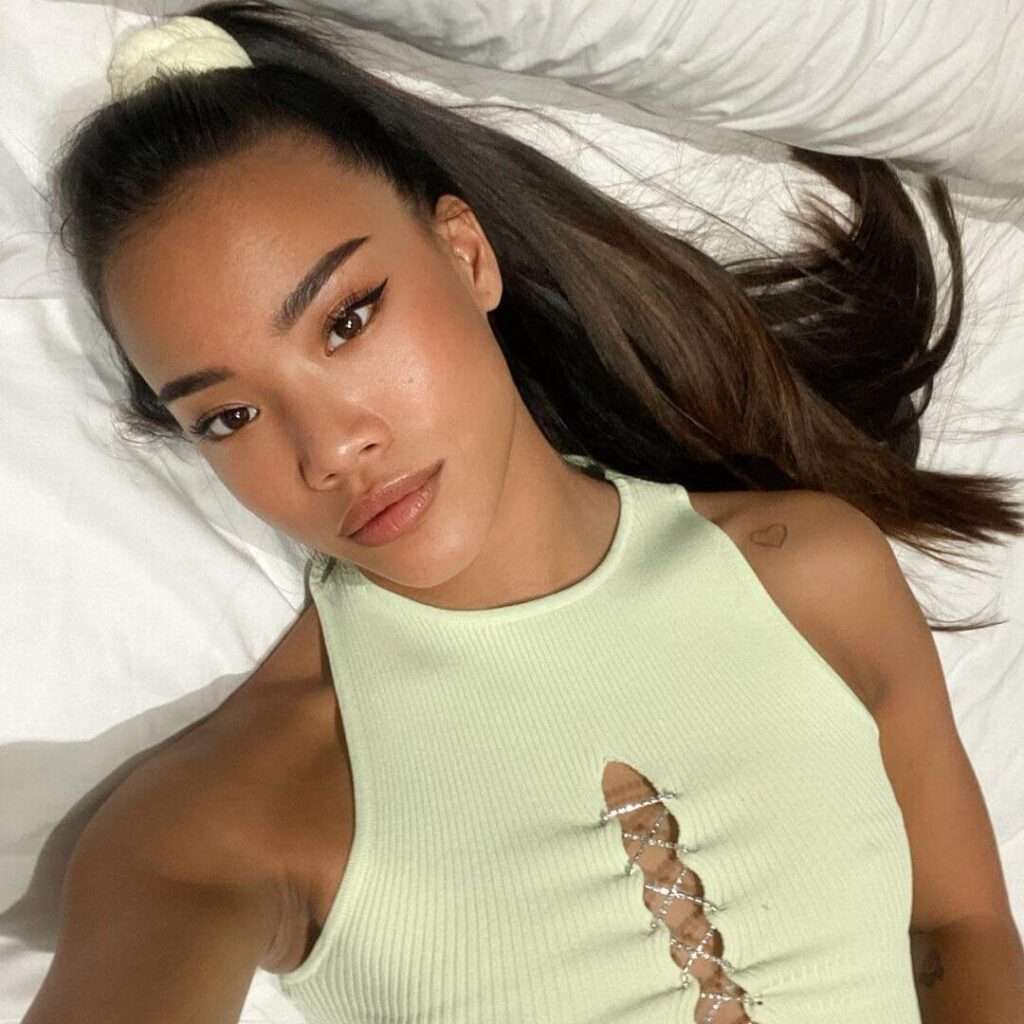Nona Sobo is wearing off white shirt and lying on bed while posing for taking the picture