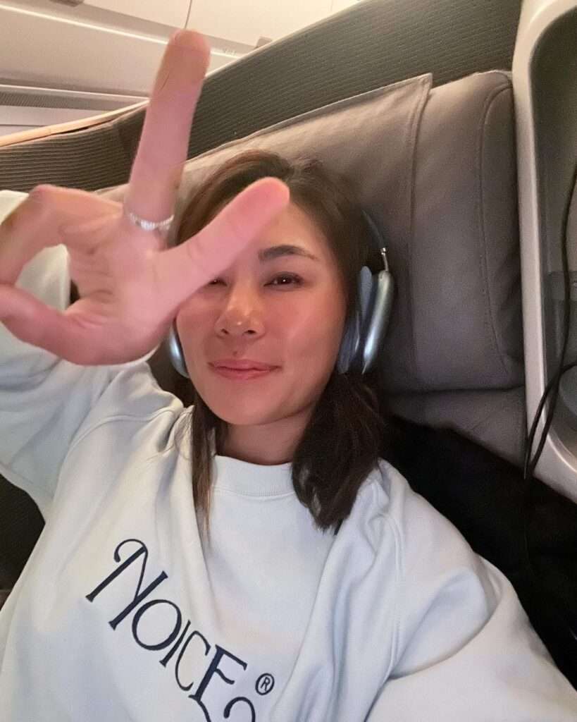 Danielle in the white printed sweatshirt while wearing headphones and showing victory sign towards camera