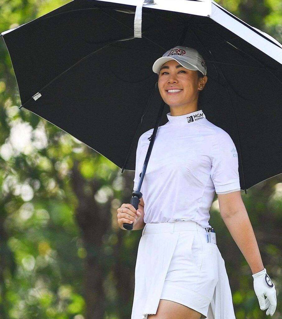 Danielle Kang in the white t-shirt pair with white mini skirt and cap while holding an Umbrella and smiling