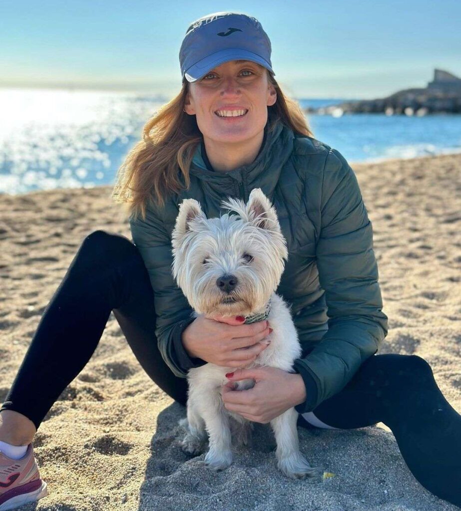 Mireia Belmonte in the green waterproof jacket pair with black pant and blue cap while holding her pup and smiling towards camera