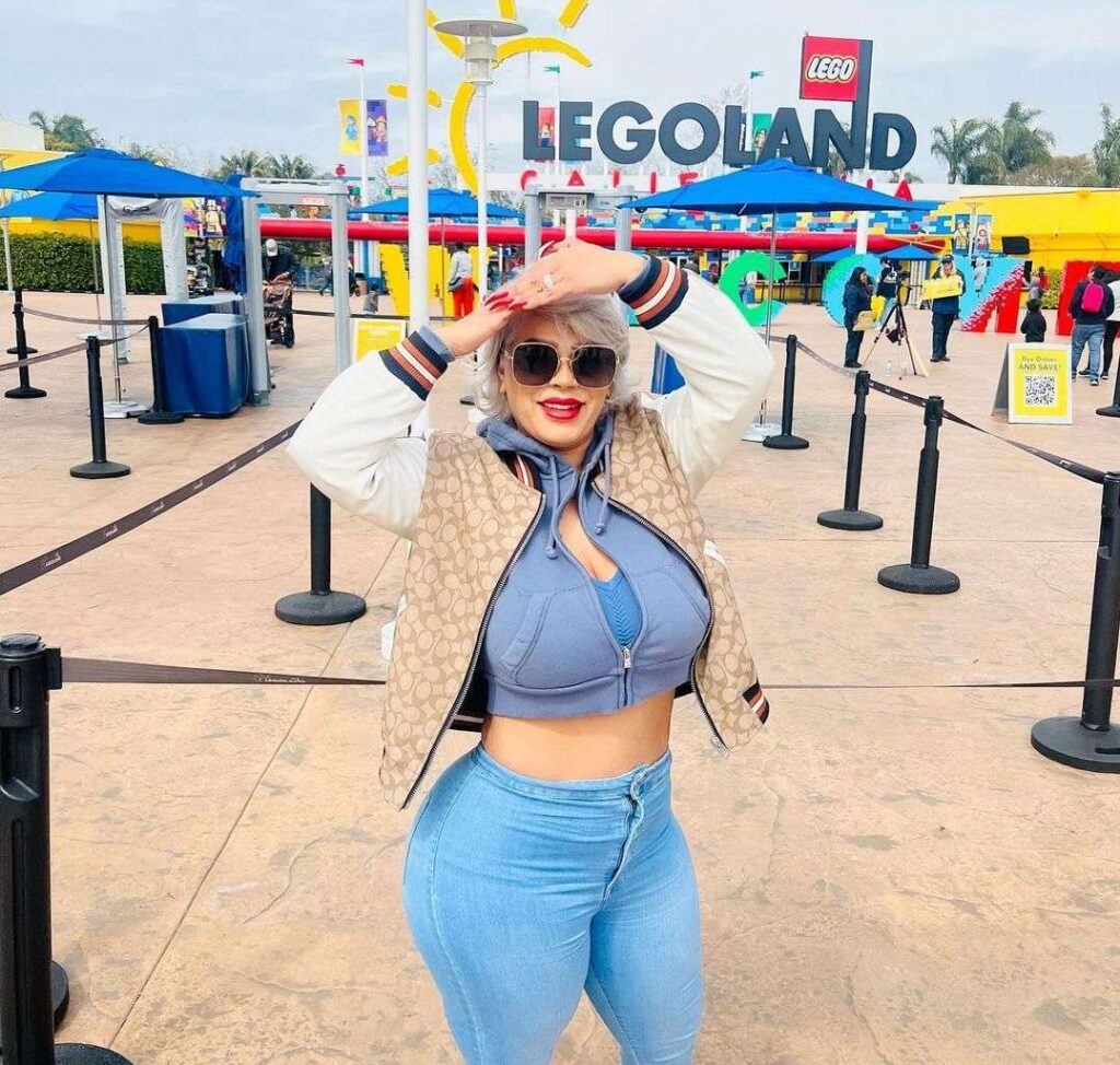 La Chula in the blue crop top with blue denim and brown jacket while poses for a photo