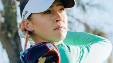 Nelly Korda in the turquoise color t-shirt pair with white pants and white cap holding a golf club in her hand and poses for a photo