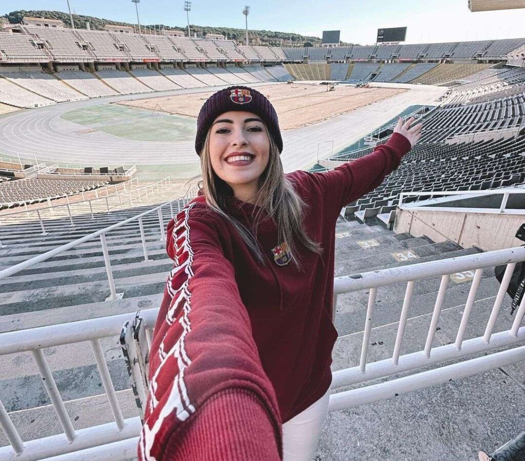Raquelcule in the maroon sweatshirt pair with white pants and black cap while taking picture in the stadium