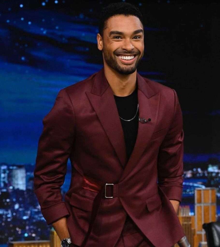 Rege Jean in the black dress shirt pair with maroon coat and dress pant while smiling towards camera