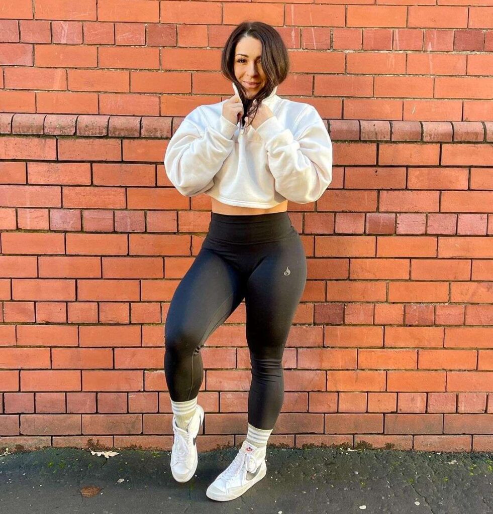 Sophie Brewster in the white sweatshirt pair with black leggings and white joggers while poses for a photo