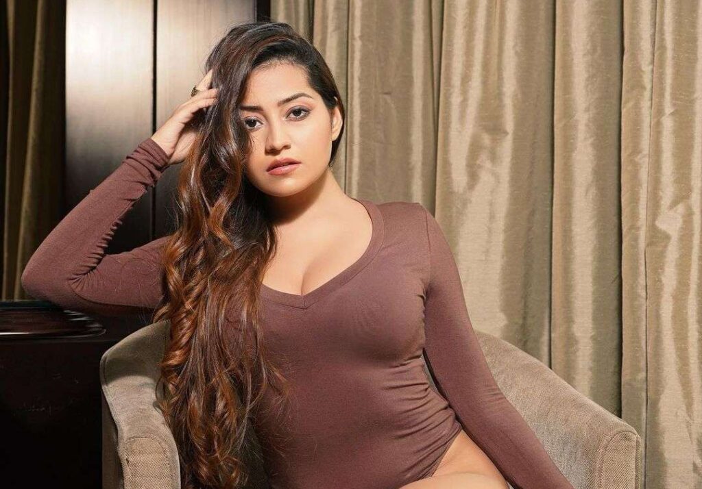 Simran Kaur in the maroon one piece outfit while sitting on the sofa and looking towards camera