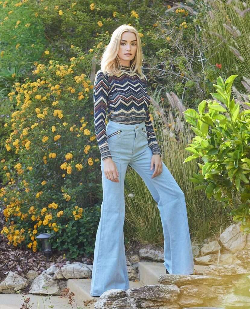 Brianne Howey is wearing colorful shirt over blue jeans or posing while taking the picture
