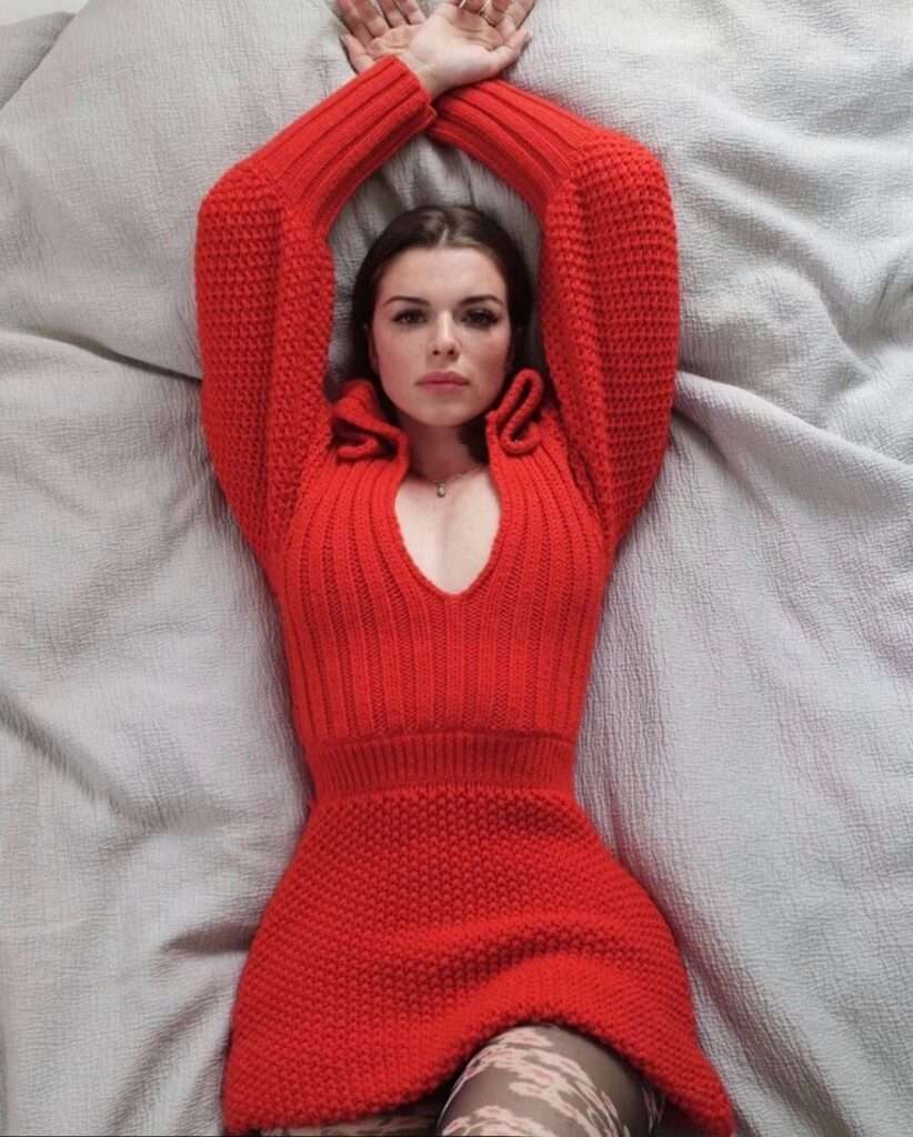 Julia Fox is wearing red dress and lying on bed while posing for the picture