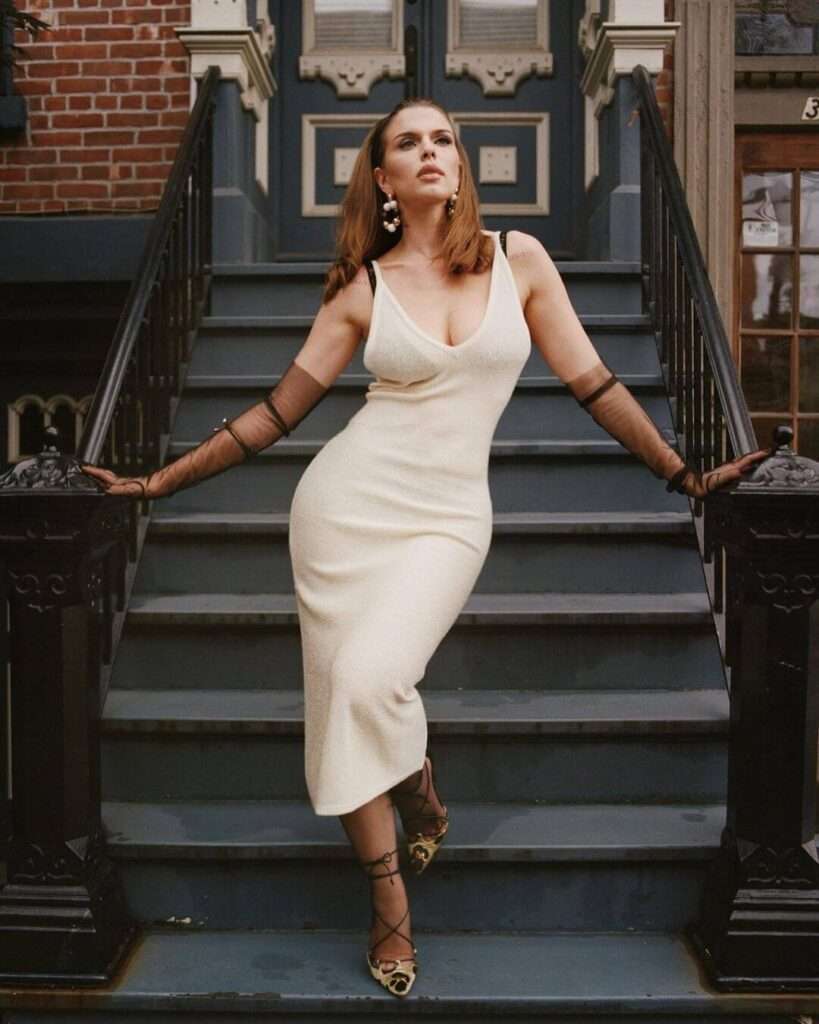 Julia Fox is wearing black bra over off white dress and standing on steps while posing for the picture