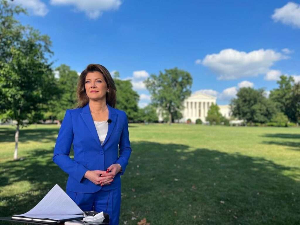 Norah O'Donnell is wearing blue pant and coat or smiling while posing for the picture