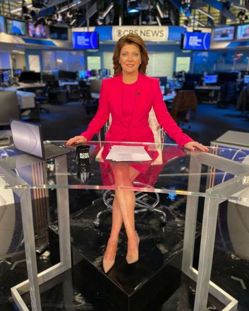 Norah O'Donnell is wearing pink shirt over coat and skirt or ready for the news broadcast or posing for the picture