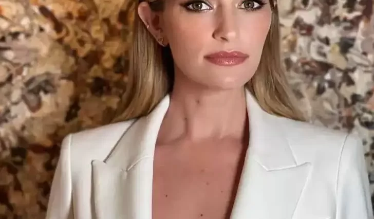 Brianne Howey is wearing white pant coat or posing while taking the picture