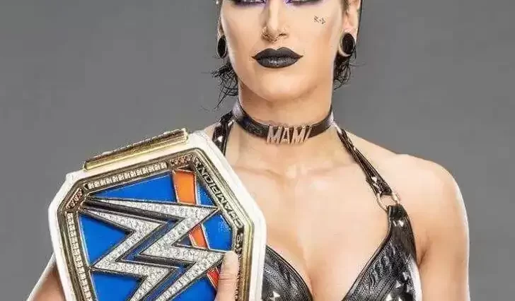 Rhea Ripley is wearing black outfit and holding the WWW Championship belt and posing while taking the picture