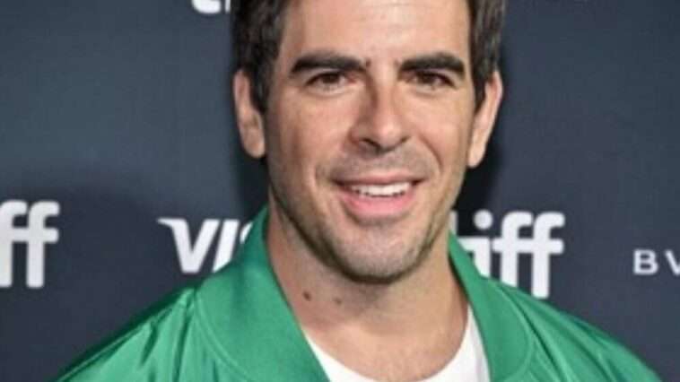 Eli Roth is wearing white shirt or green shirt and posing while taking the picture