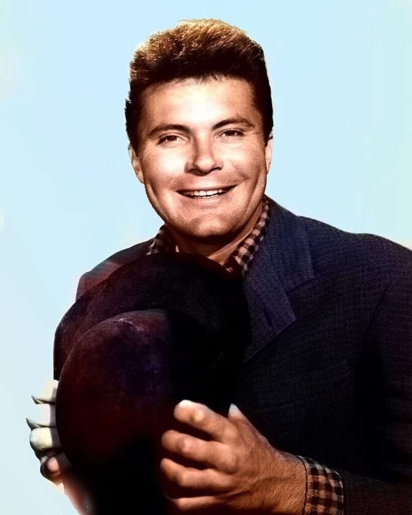 Max Baer Jr is wearing pant coat and holding the cap or smiling while posing for the picture