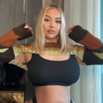 Confident plus-size model with blonde hair posing indoors in a stylish multicolor knit shrug over a black crop top, showcasing body positivity and modern fashion.