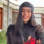 Victoria Hernández standing outdoors in front of a modern house, smiling brightly with a black headscarf and shredded black top.
