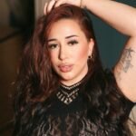 Close-up portrait of kdreemz with voluminous wavy hair and a confident gaze, revealing her tattoo and empowering beauty presence.