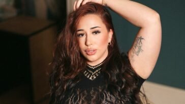 Close-up portrait of kdreemz with voluminous wavy hair and a confident gaze, revealing her tattoo and empowering beauty presence.