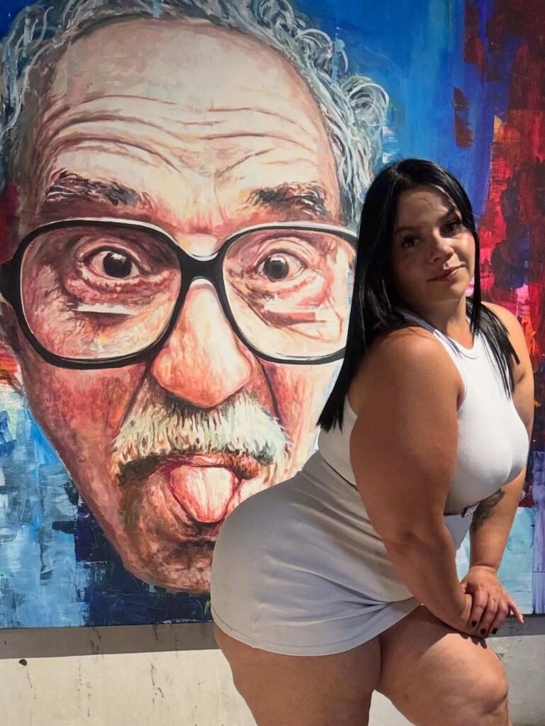 Colombian plus-size influencer Yurley Rúa posing in a short white dress in front of a colorful Gabriel García Márquez mural.