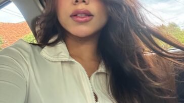 Close-up selfie of Angel Lopez wearing a white zip-up top with loose hair in a car.
