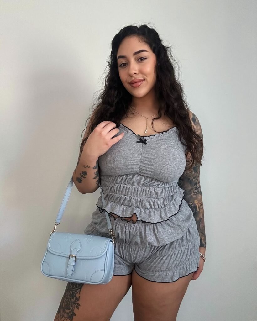 Kat Tori posing in a grey ruched lounge set with a light blue handbag, showcasing casual chic fashion.