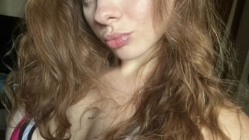 Shawnee Youngblood taking a close-up selfie in a pink and white low-cut top, showcasing her natural makeup and wavy hair.