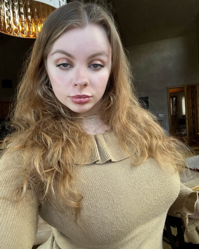 Shawnee Youngblood taking an indoor selfie wearing a beige knit sweater, with loose wavy hair and a natural beauty look.